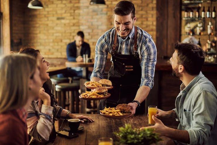 Garçom sorrindo servindo pratos a um grupo de amigos numa mesa do restaurante